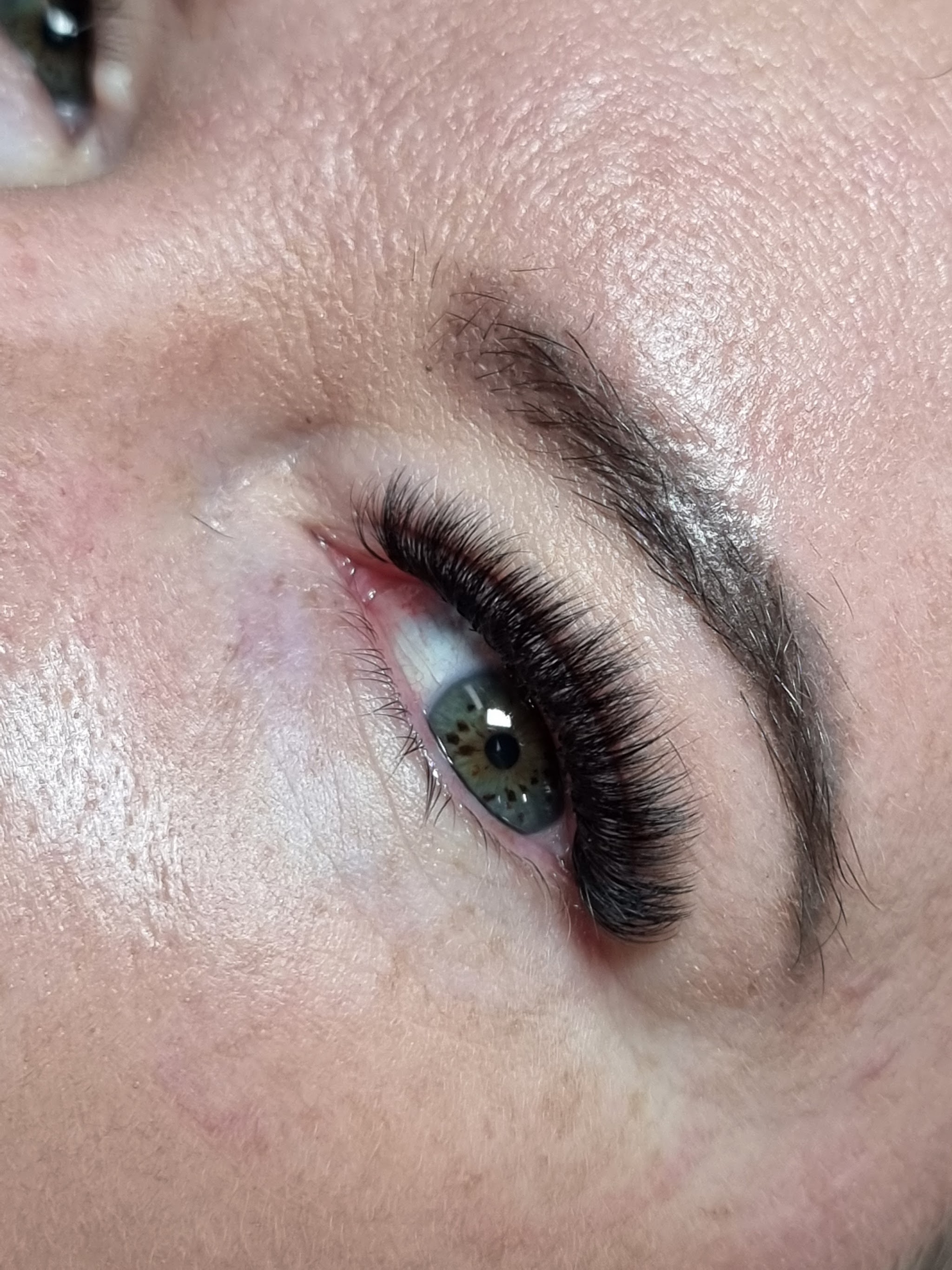 Close-up of a full set of dark lash extensions on a green eye