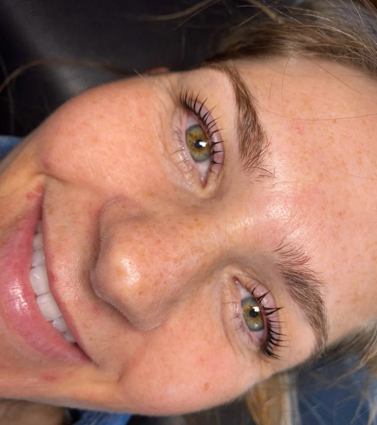 A smiling client with lifted, curled natural lashes after a lash lift